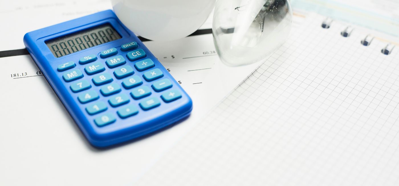 Calculadora, lâmpada e caderno sobre uma fatura de eletricidade